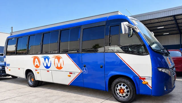 Micro-ônibus da AWM, azul e branco com a logo na lateral, estacionado sob céu aberto